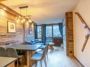 A modern interior with a wooden wall, a dining area with a long table and chairs, a sofa, and a ski rack. - Elegant apartment, pets welcome - 4 guests (Val-d'Isère)