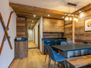 A modern kitchen with wooden accents, a dining area with blue chairs, and a visible staircase leading to another room. - Elegant apartment, pets welcome - 4 guests (Val-d'Isère)