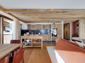 A modern kitchen with wooden cabinets, a dining area with a wooden table and chairs, and a cozy seating area with a sofa. - Val d'Isère - Spacious 109 m² Chalet for 8 (Val-d'Isère)