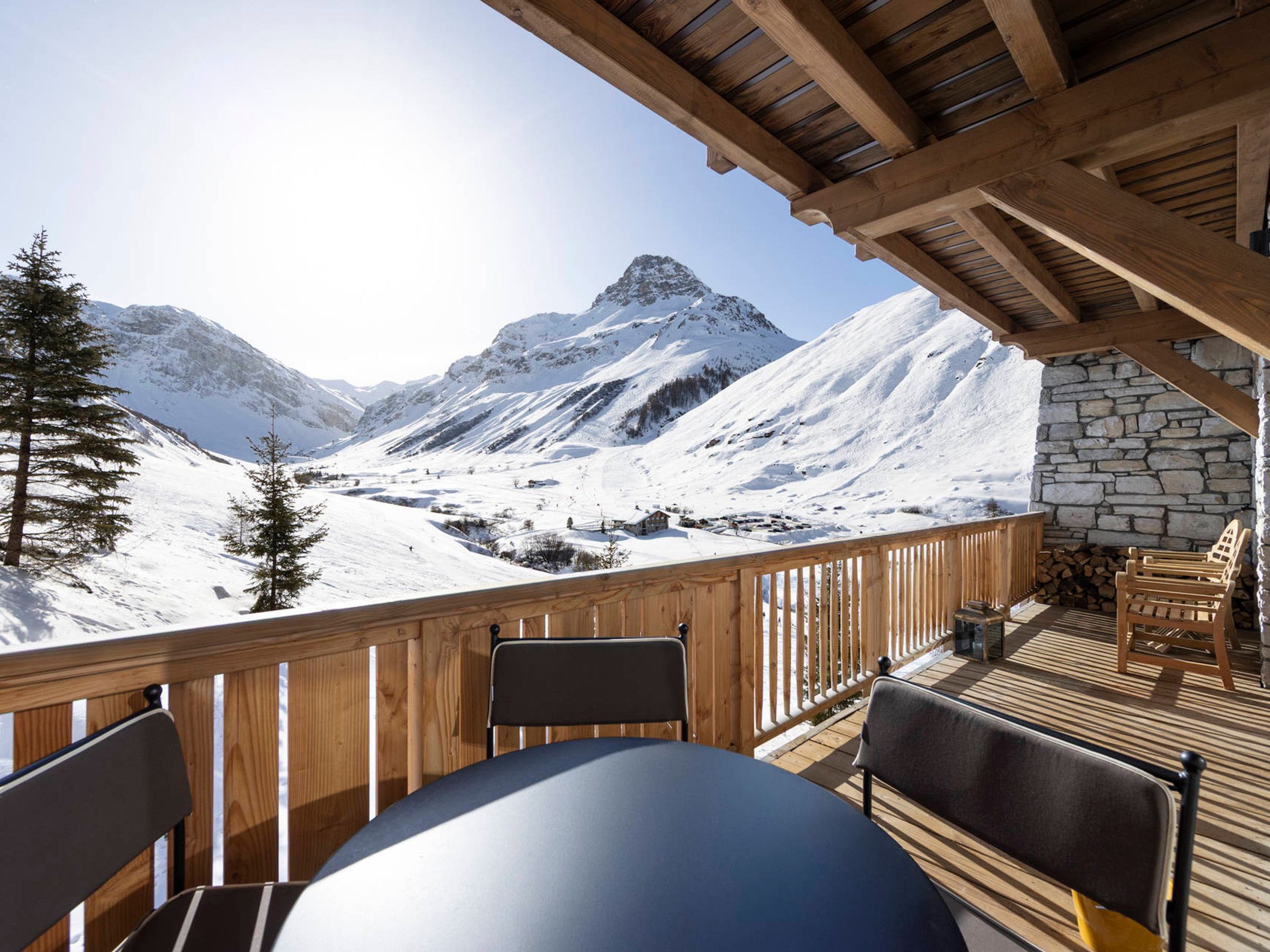 A wooden deck with a table and chairs, overlooking a snowy mountain landscape.