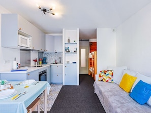 Um espaço compacto com cozinha compacta, área de refeições e sofá com almofadas coloridas.