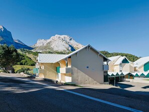 Um edifício com telhado plano e uma pequena construção anexa, com montanhas ao fundo.