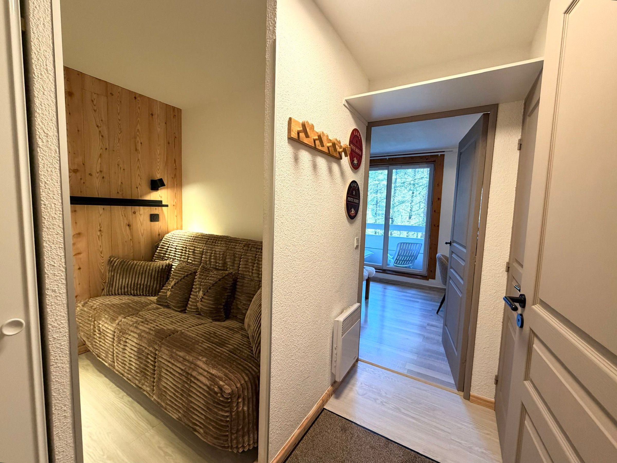 A room with a wooden wall, a sofa, a radiator, and a door leading to a balcony.