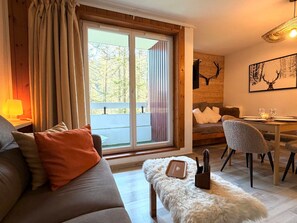 A cozy living room with a sofa, a dining table with chairs, a fireplace, and a large window with curtains. - Mountain studio tranquility, 5 guests (Vars)