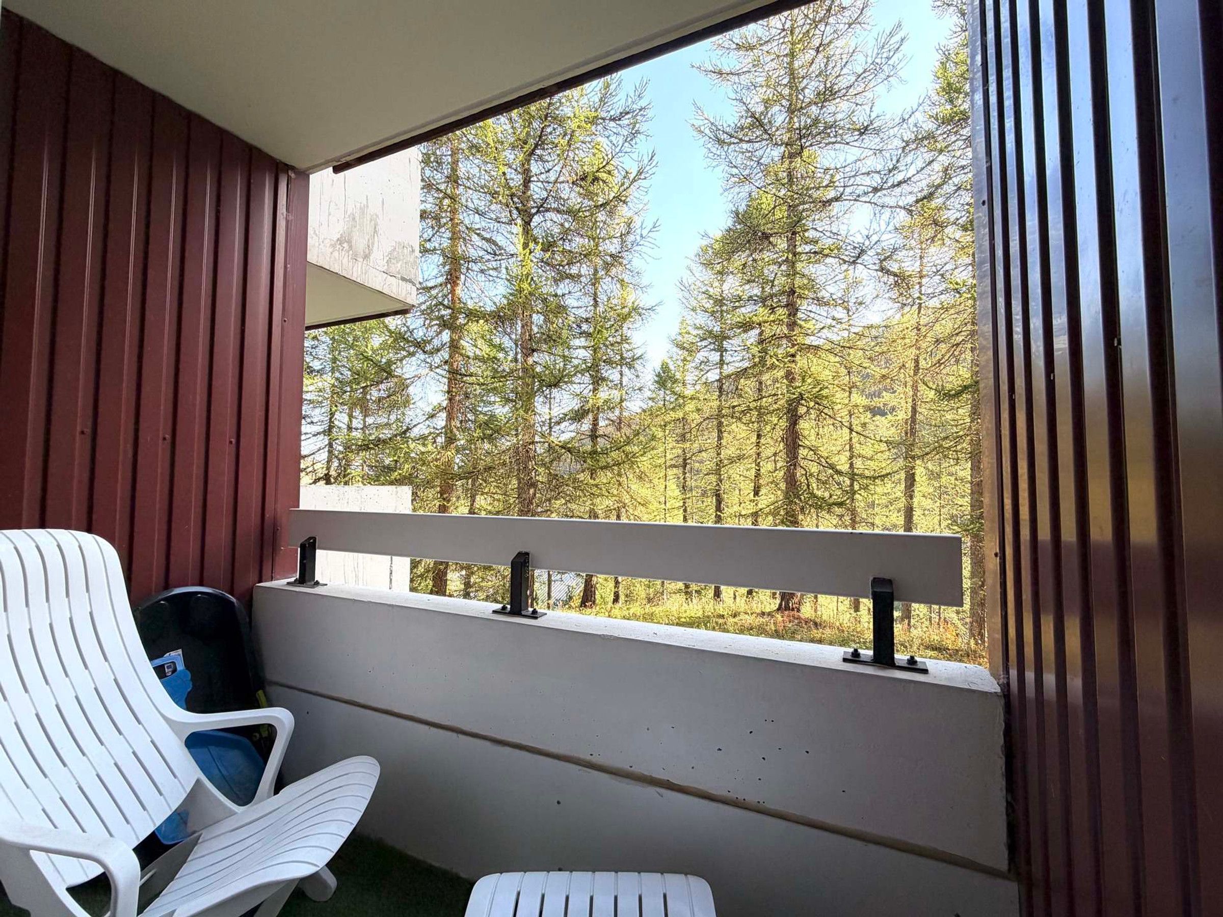 A balcony with a white chair and a small table, overlooking a forested area.