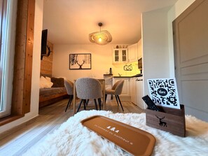 Un salon chaleureux avec un tapis blanc et moelleux, un buffet en bois doté d’un code QR et un coin repas avec des chaises et une table.