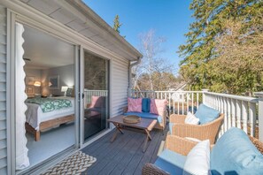 A covered deck with outdoor furniture, a sliding glass door leading to a bedroom, and a view of trees and sky.
