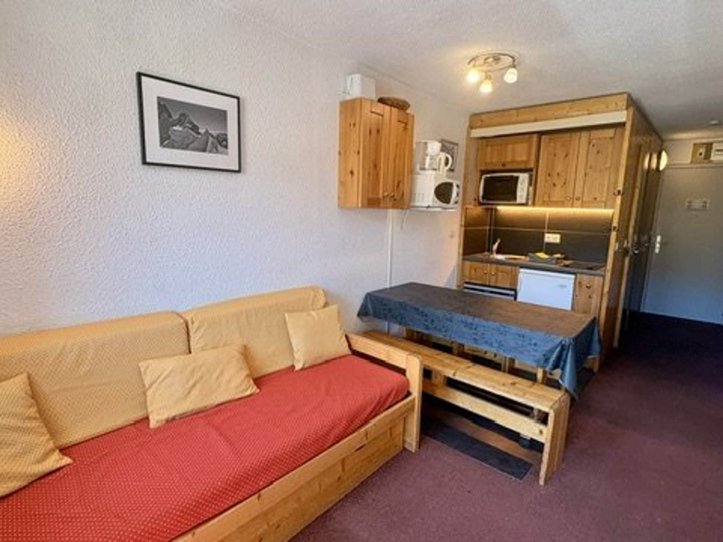 Een knus woongedeelte met een bank, een klein tafeltje, een kitchenette en een magnetron.