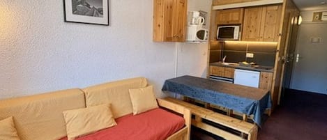 Un espace de vie compact comprenant un canapé, une petite table, un coin cuisine et un four à micro-ondes.
