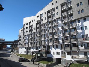A multi-story residential building with balconies, a covered entrance, and a parking area. - Apartment with balcony - 4 guests, south view (Val Thorens)