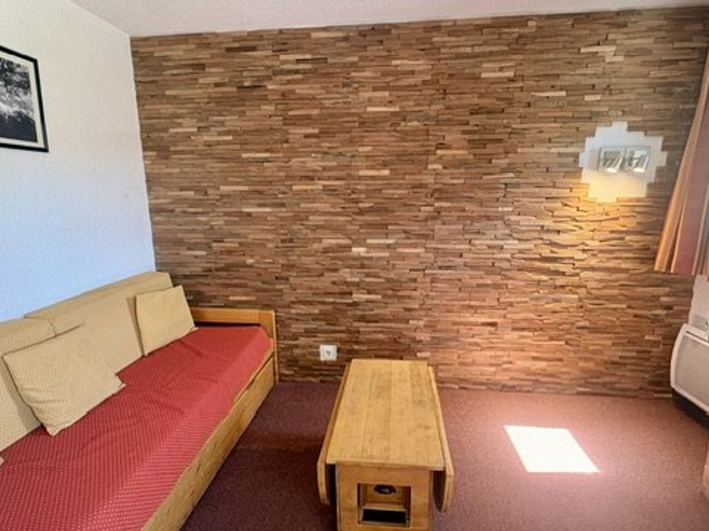 Quarto com parede de madeira, sofá vermelho e um banco de madeira.