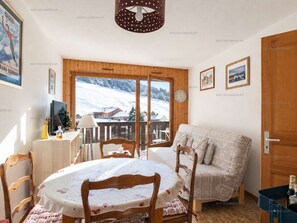 Ein gemütliches Zimmer mit Holztisch, Stühlen, einer Couch und einem großen Fenster mit Blick auf Schnee.
