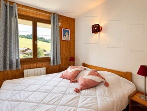 Ein Schlafzimmer mit einem großen Bett, Holzwänden, einem Fenster mit Vorhängen, einer Nachttischlampe und einem gerahmten Bild an der Wand.