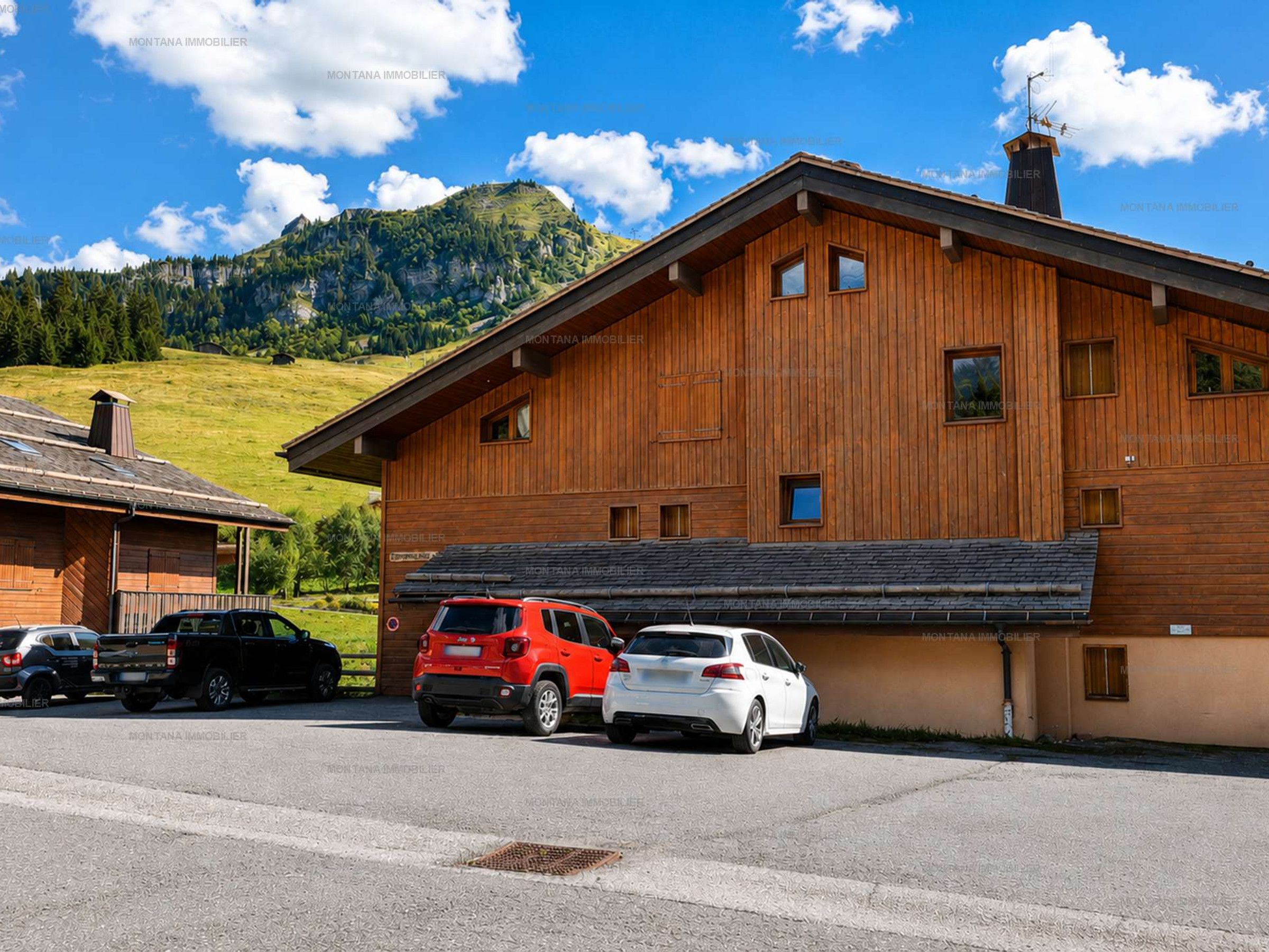 Un bâtiment en bois avec un toit en pente, un garage pouvant accueillir deux voitures et un paysage montagneux en arrière-plan.