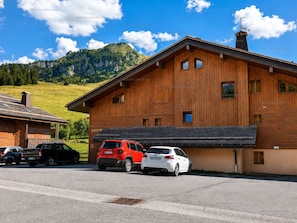 Ein Holzhaus mit geneigtem Dach, eine Garage mit zwei Autos und eine Bergkulisse im Hintergrund.
