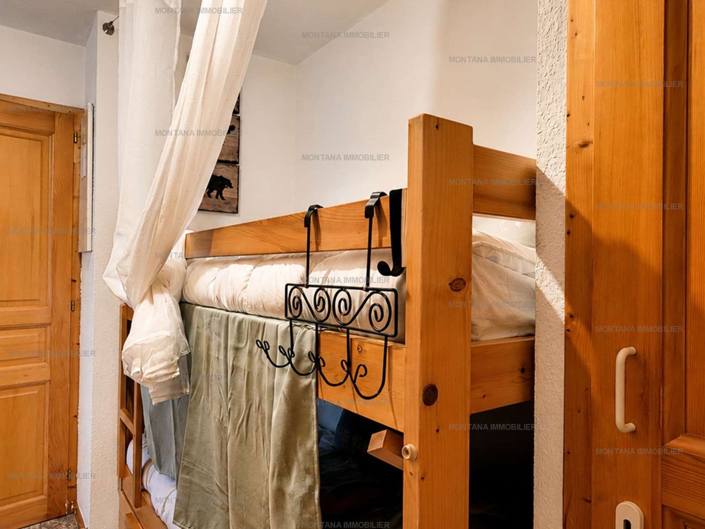A wooden bunk bed with a headboard, a curtain, and a wall-mounted hook.
