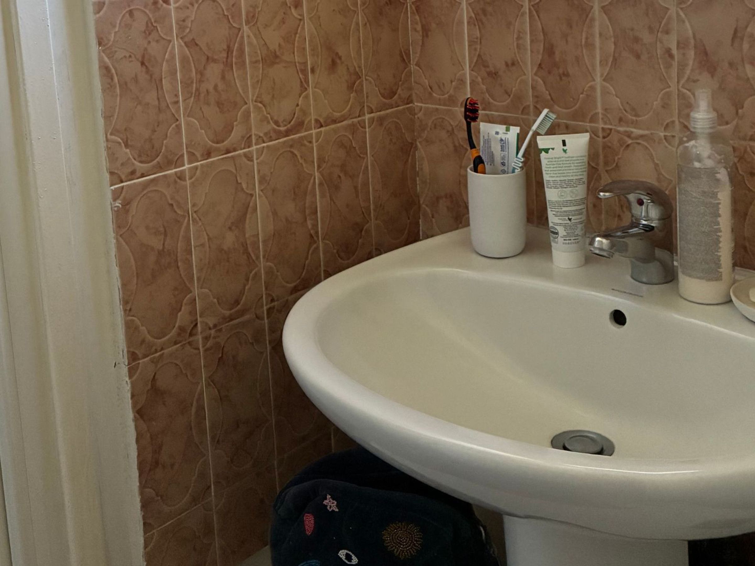 Ein Badezimmer mit einem weißen Waschbecken, einem Zahnputzhalter mit Zahnbürsten, Zahnpasta und einer Handseifenflasche.