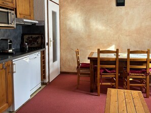 A compact kitchen with a microwave, toaster, and dishwasher. There is a wooden dining table with chairs and a small wooden bench. - Cozy apartment - 4 guests (Valloire)