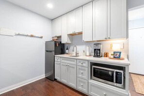 Una cocina con armarios blancos, horno empotrado, cafetera y refrigerador.
