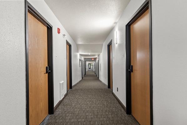 A hotel hallway with carpeted floors, wooden doors, and wall-mounted light fixtures.