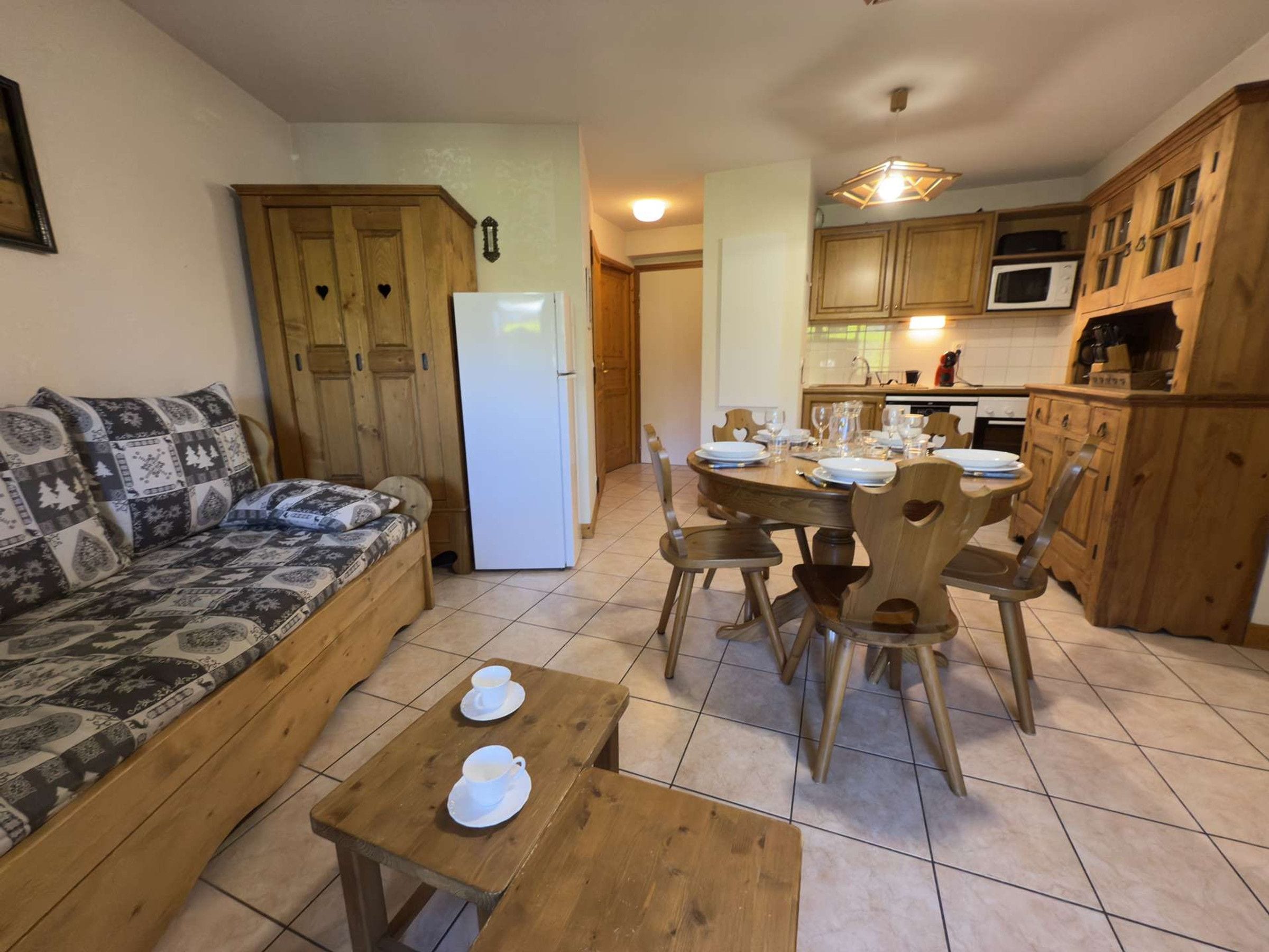 A cozy living area with a sofa, a dining table set for four, and a kitchen with wooden cabinets and a refrigerator.