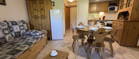 A cozy living area with a sofa, a dining table set for four, and a kitchen with wooden cabinets and a refrigerator.