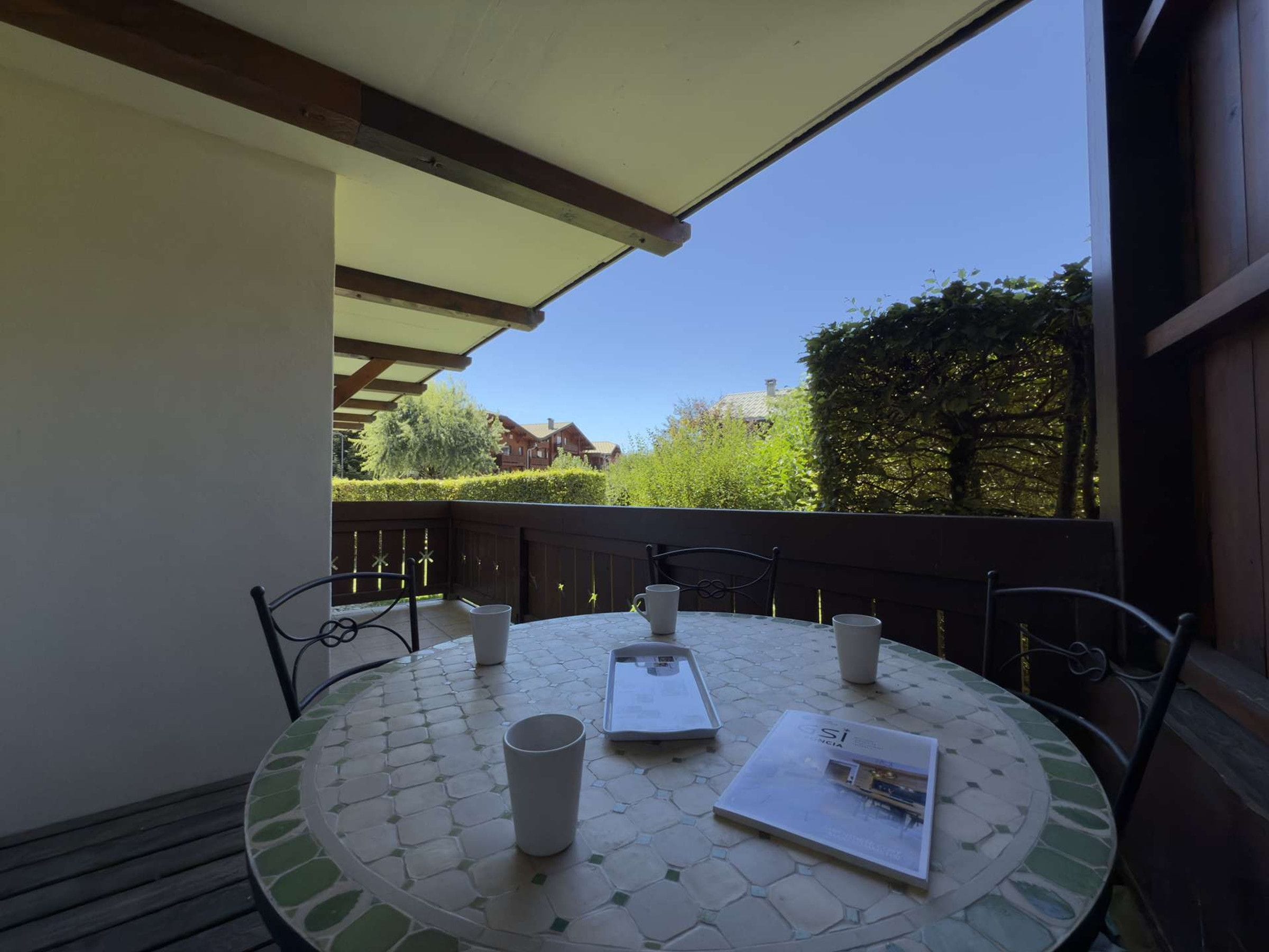 En udendørs terrasse med et rundt bord, fire stole og en hvid parasol.