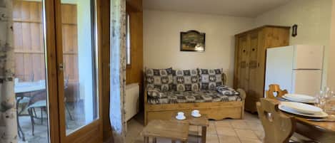 A cozy living room with a sofa, a small wooden table, and a dining area with chairs and a table set for two.