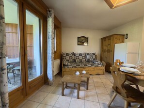 A cozy living room with a sofa, a small wooden table, and a dining area with chairs and a table set for two. - Practical apartment, private parking - 6 guests (Praz-sur-Arly)
