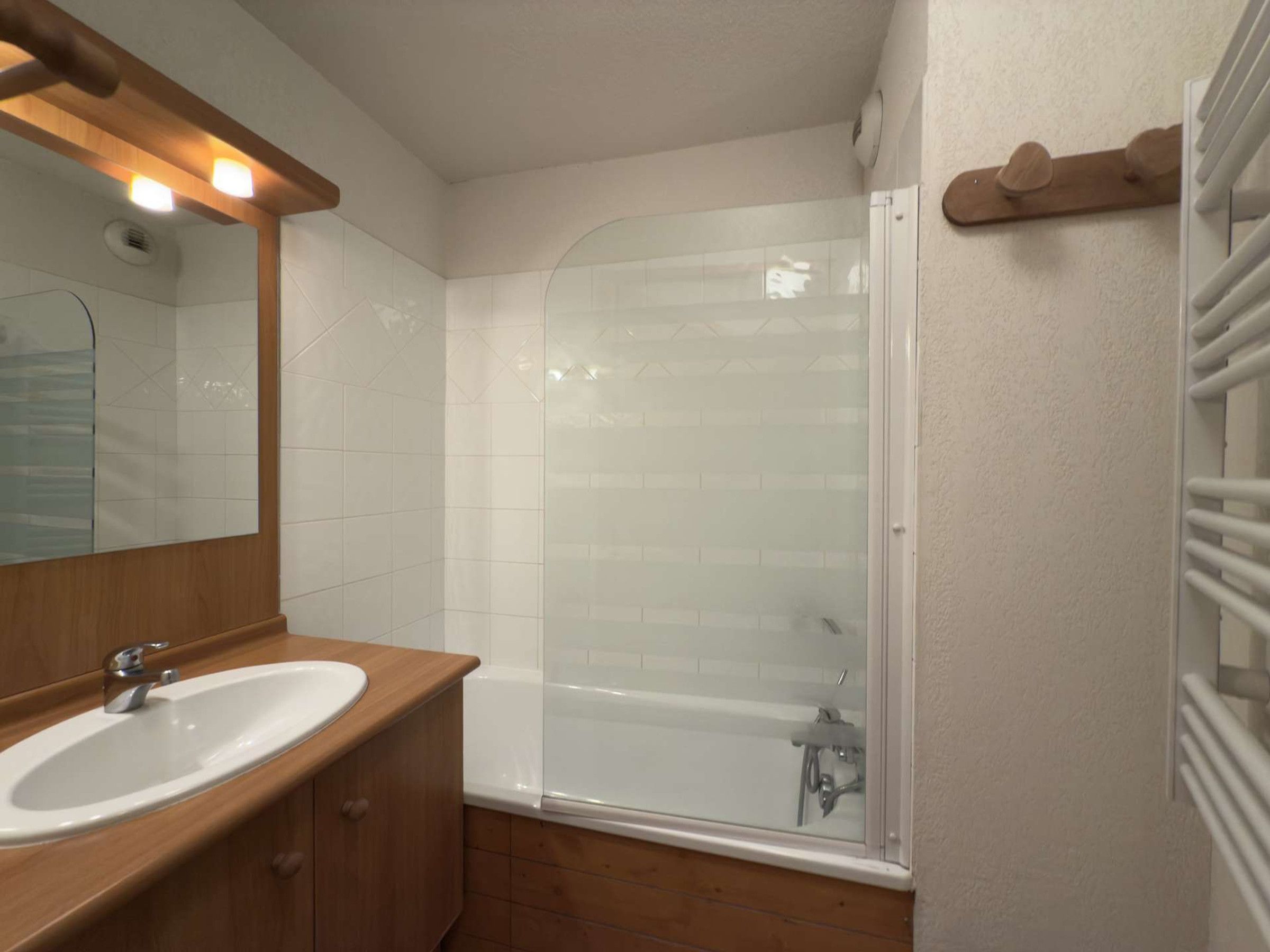 Un baño con tocador de madera, lavabo blanco, cerramiento de ducha de vidrio y un perchero para toallas.