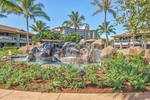 Ein Resort mit Wasserspiel, darunter ein Wasserfall und ein Pool, umgeben von Palmen und einem Gebäude mit Balkonen.