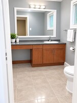 Un baño con tocador, lavamanos, espejo e inodoro.