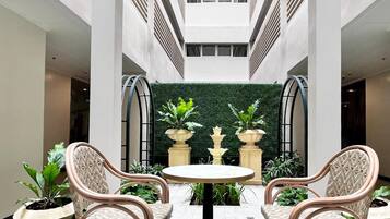 A courtyard with two wicker chairs and a table, surrounded by potted plants and a green wall.