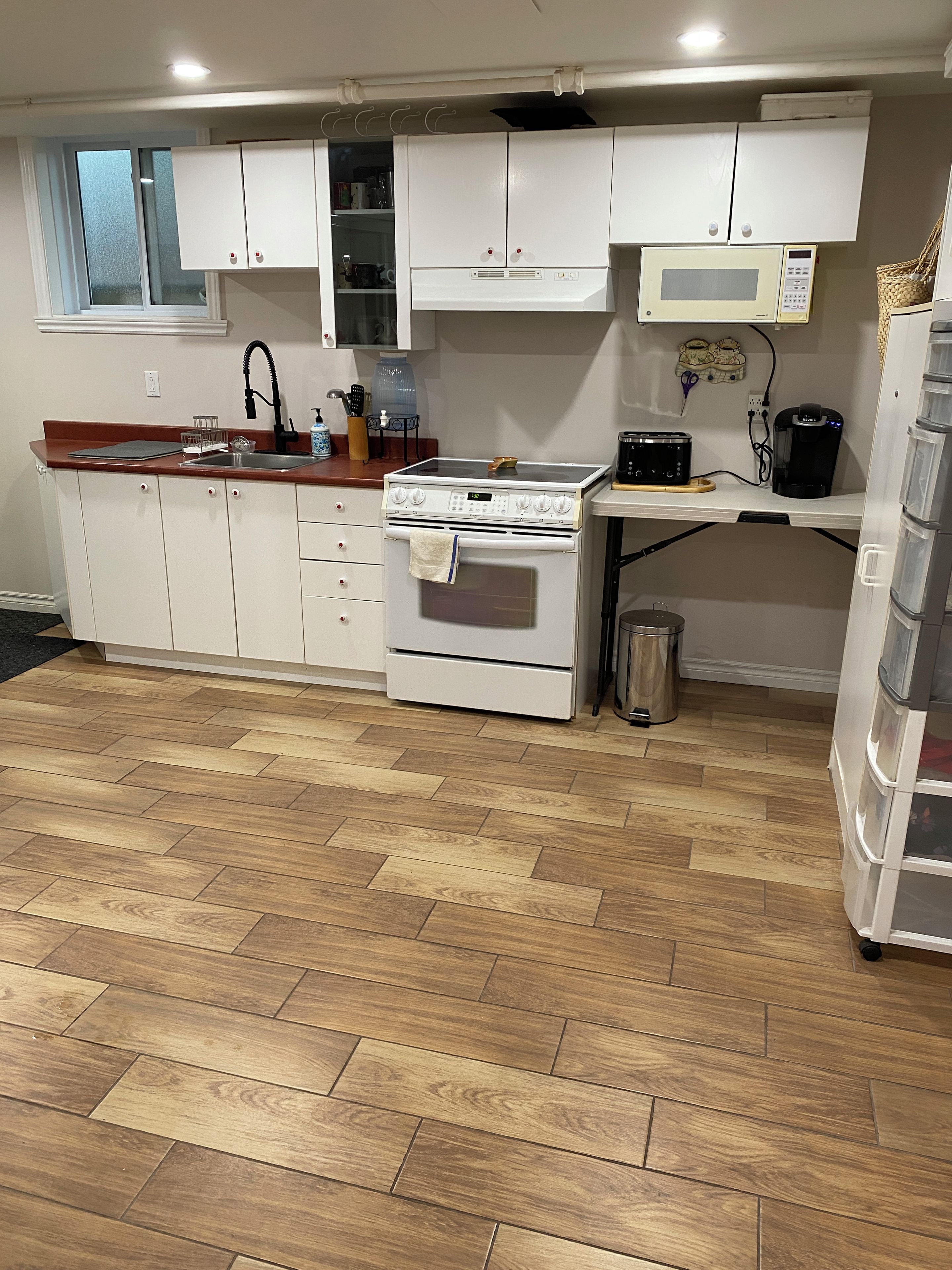 A kitchen with white cabinets, a stove, a microwave, and a sink.