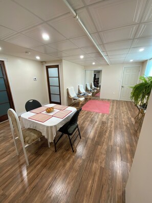 Ein Zimmer mit Esstisch, Stühlen, einem roten Teppich und einem Blumentopf.