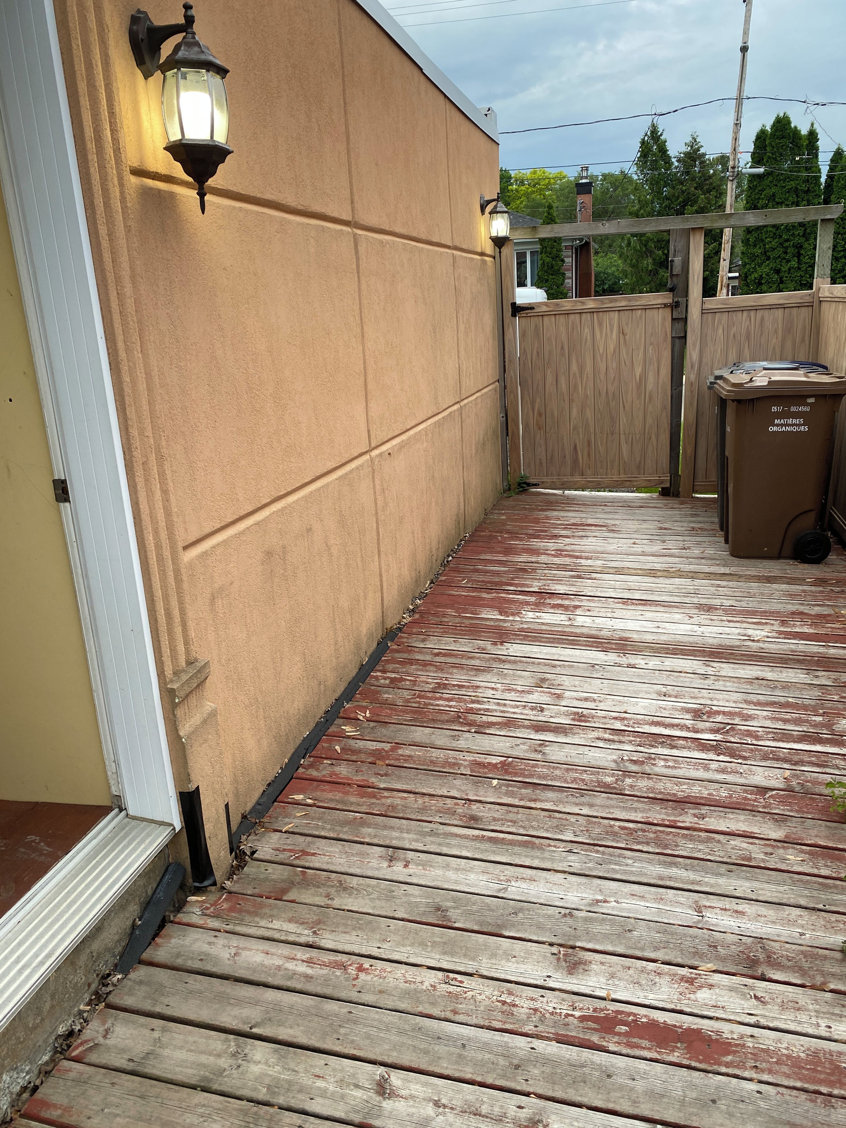 A wooden deck with a beige wall and two wall-mounted lights.