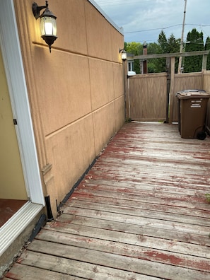 Eine Holzterrasse mit einer beigen Wand und zwei Wandleuchten.
