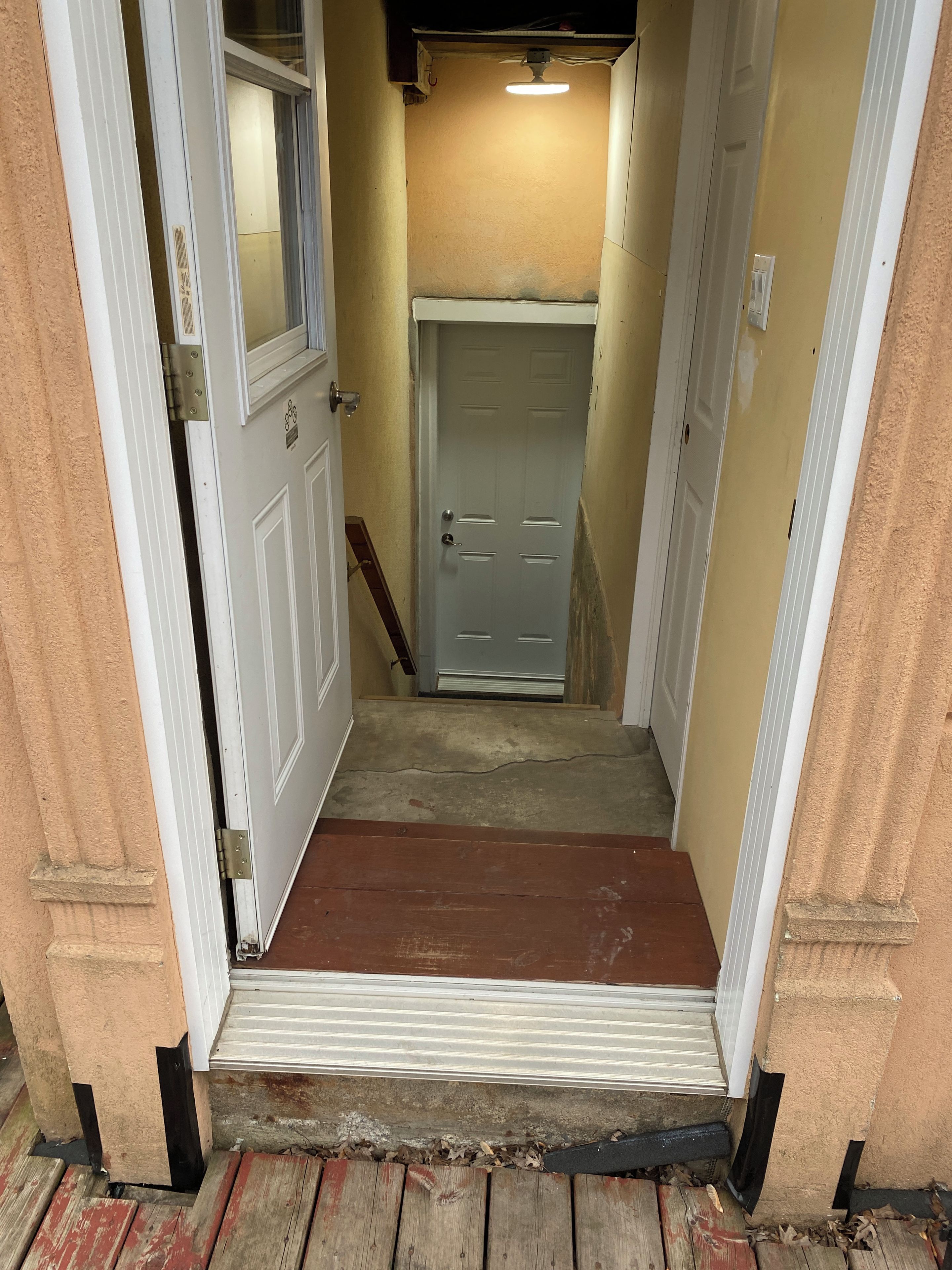 A narrow hallway with a wooden door at the end, a small step leading up to it, and a light fixture above.
