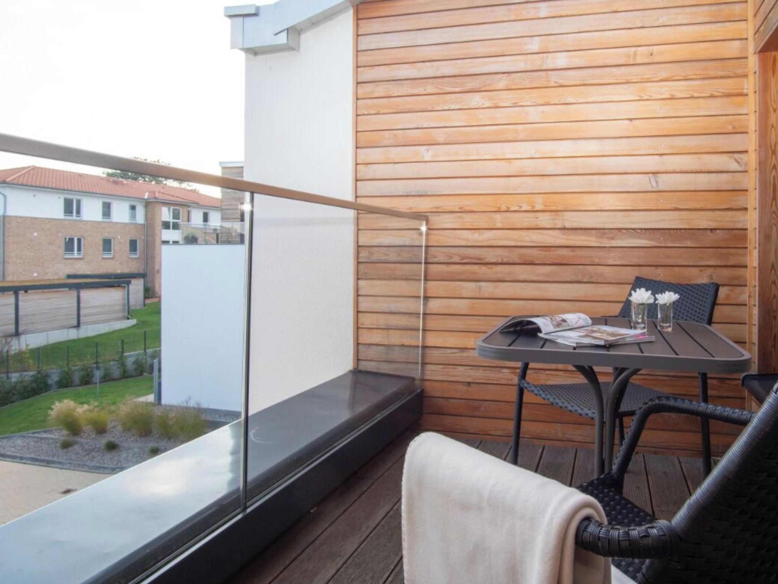 A balcony with a glass balustrade, a table with chairs, and a view of a residential area.