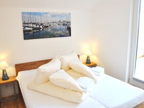 Een hotelkamer met een bed, twee bedlampen, een schilderij van een jachthaven en een raam.