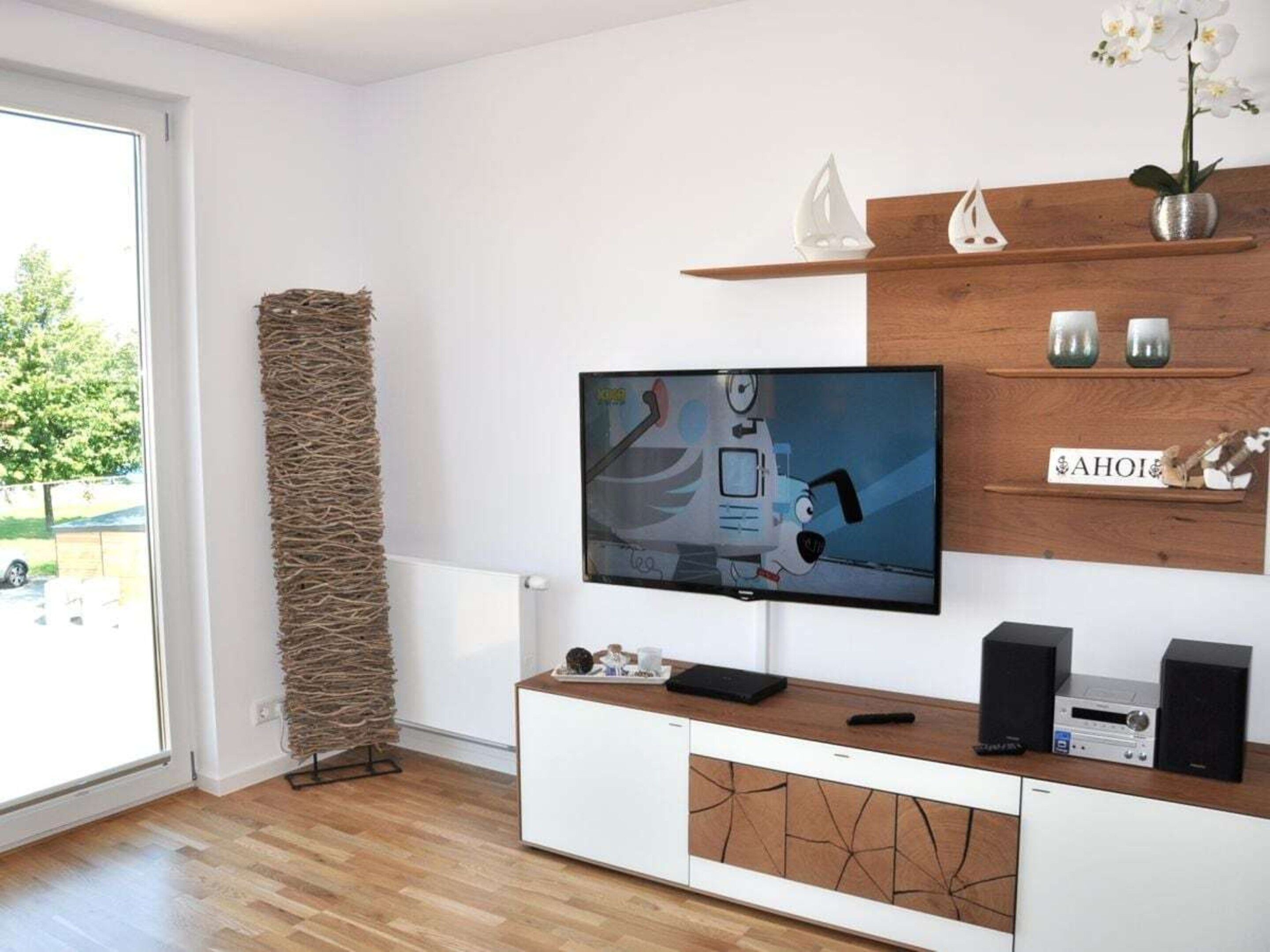 A modern living room with a flat-screen TV, wooden flooring, a white cabinet, and a decorative wall piece.