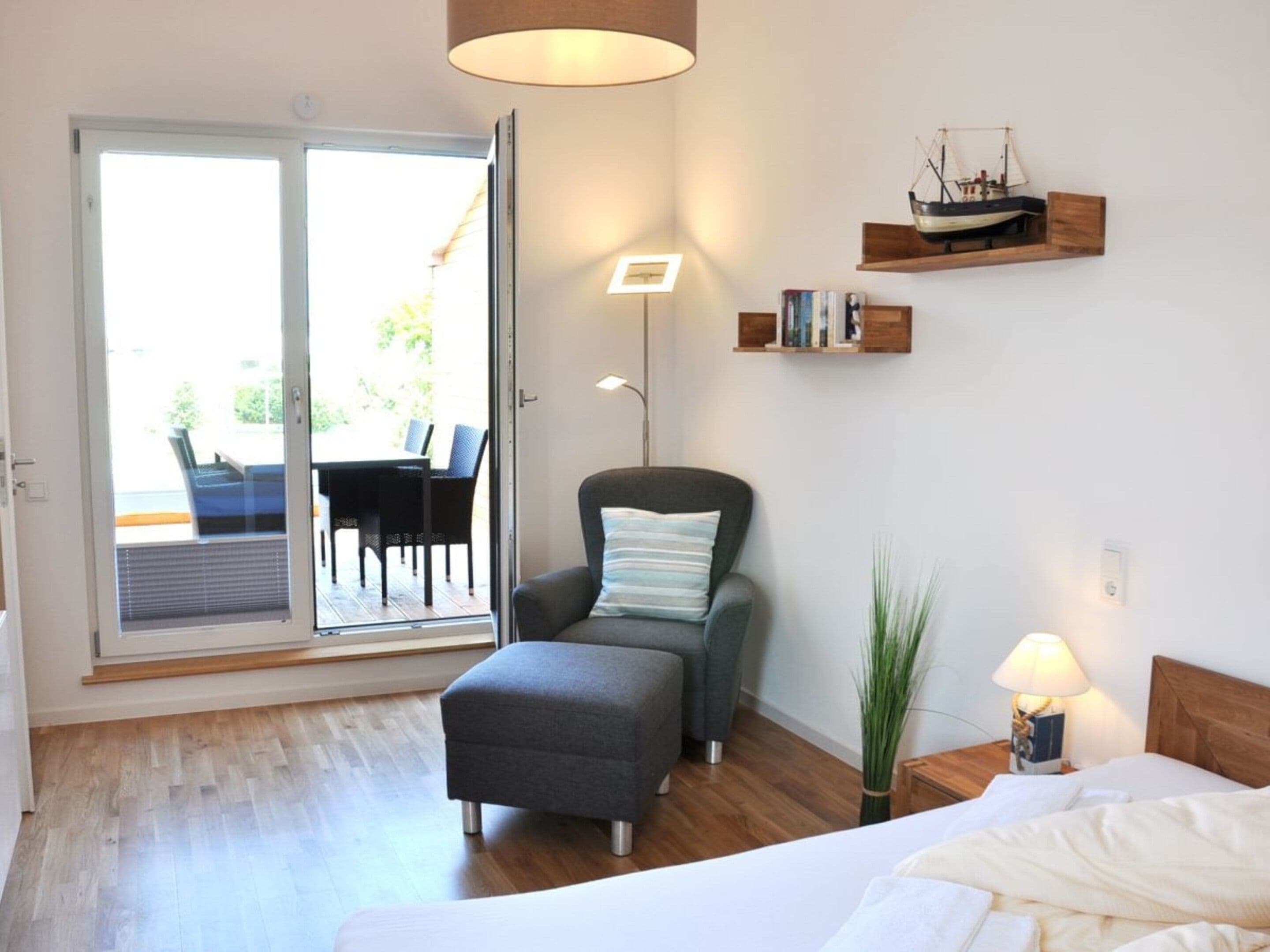 A bedroom with a bed, a chair, a bedside table, a lamp, a window, and a view of an outdoor patio.