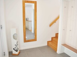A hallway with a wooden staircase, a white wall, and a mirror. - Holiday Apartment With 2 Bedrooms (Heiligenhafen)