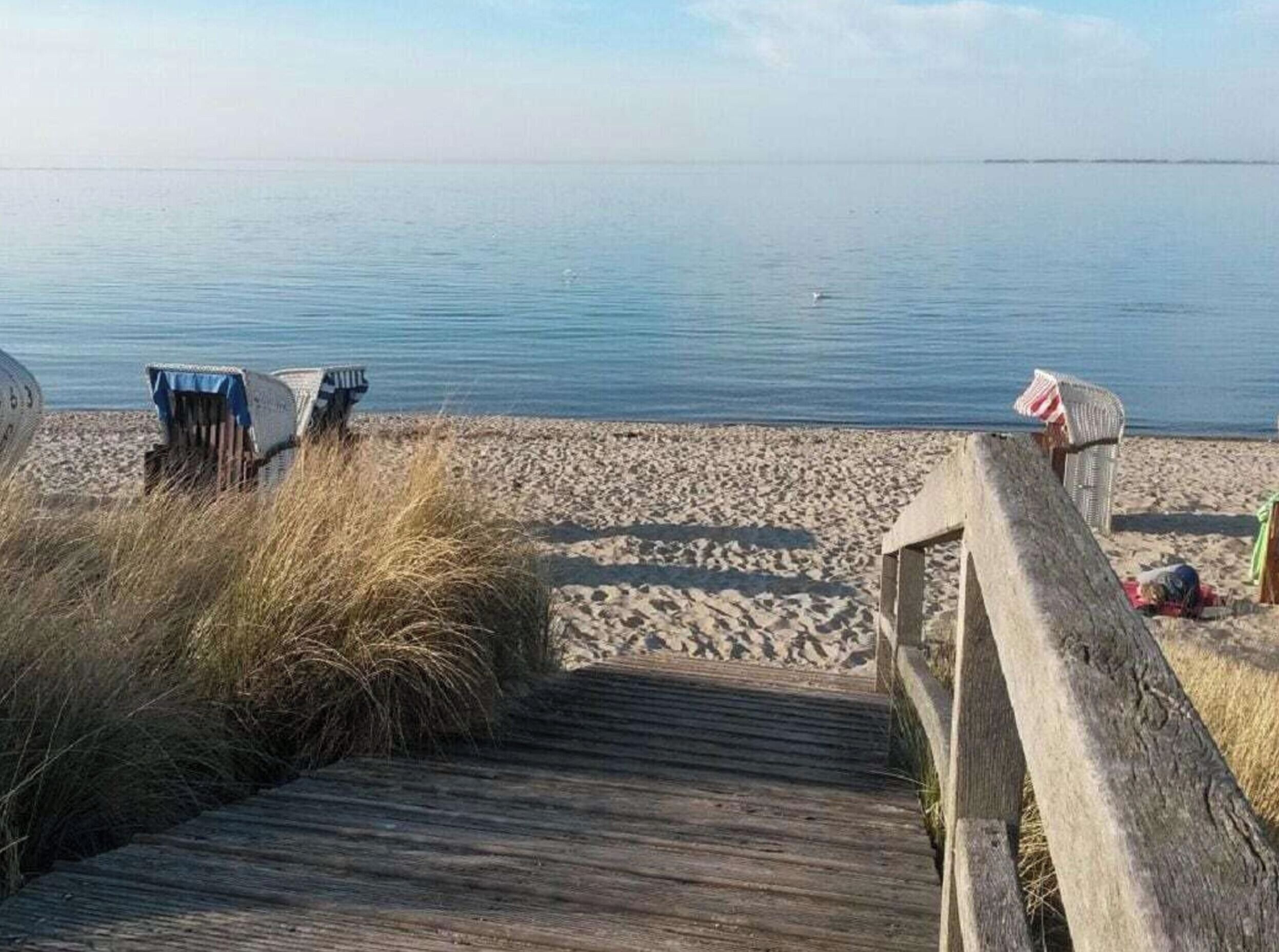 Een houten looppad dat naar een zandstrand leidt, met een rustige zee op de achtergrond.