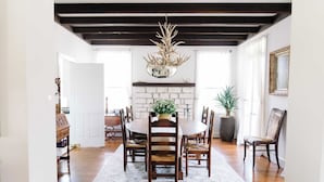 A dining room with a white brick fireplace, wooden chairs, a round table, and a chandelier with antlers. - NEW | Wisteria Ranch | Perfect Round Top Escape (Round Top)