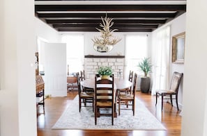 A dining room with a white brick fireplace, wooden chairs, a round table, and a chandelier with antlers. - NEW | Wisteria Ranch | Perfect Round Top Escape (Round Top)