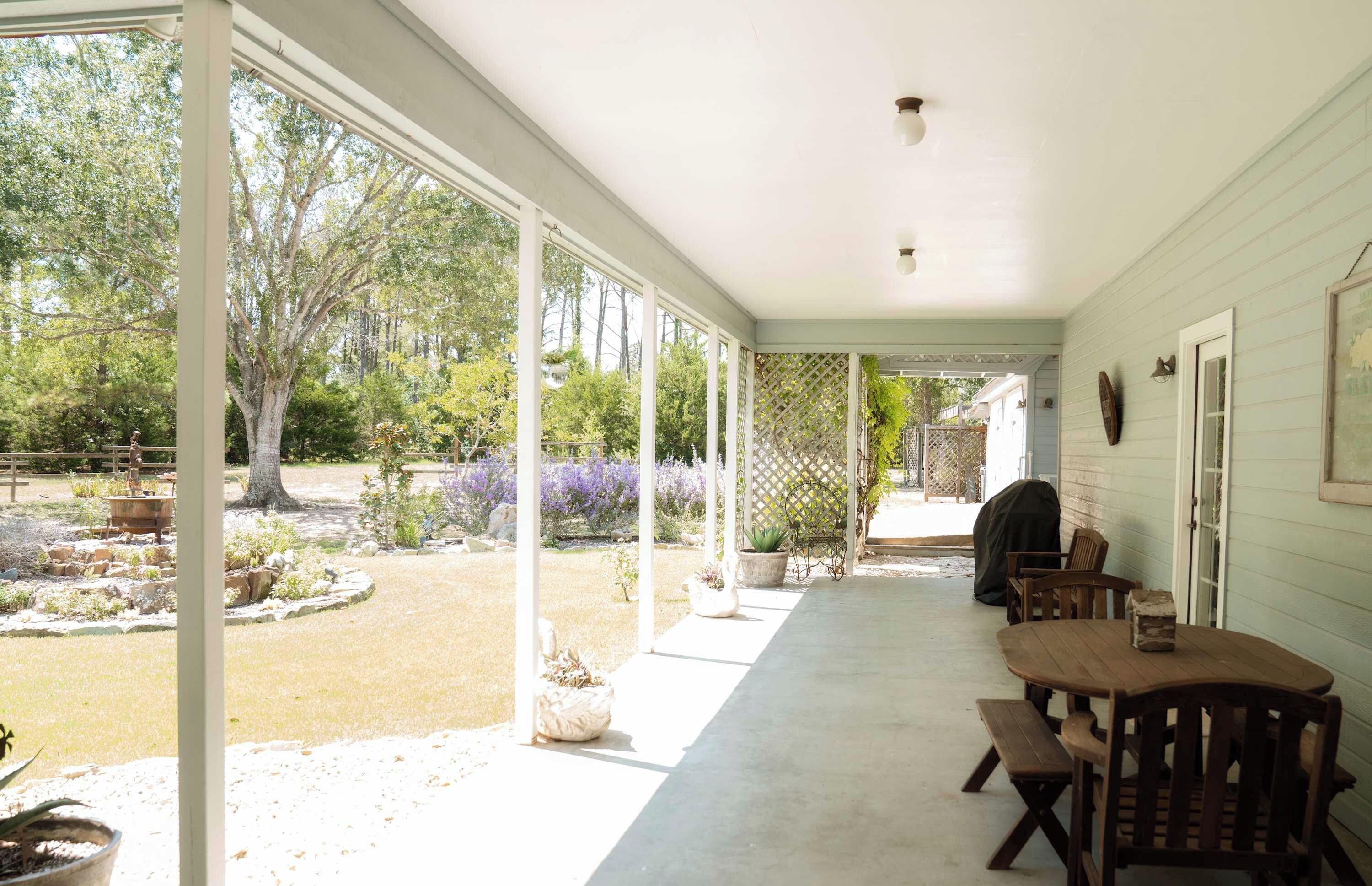 A covered patio with a table and chairs, a wooden fence, and a garden with trees and plants.