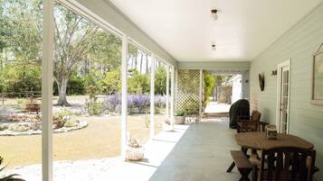 A covered patio with a table and chairs, a wooden fence, and a garden with trees and plants.