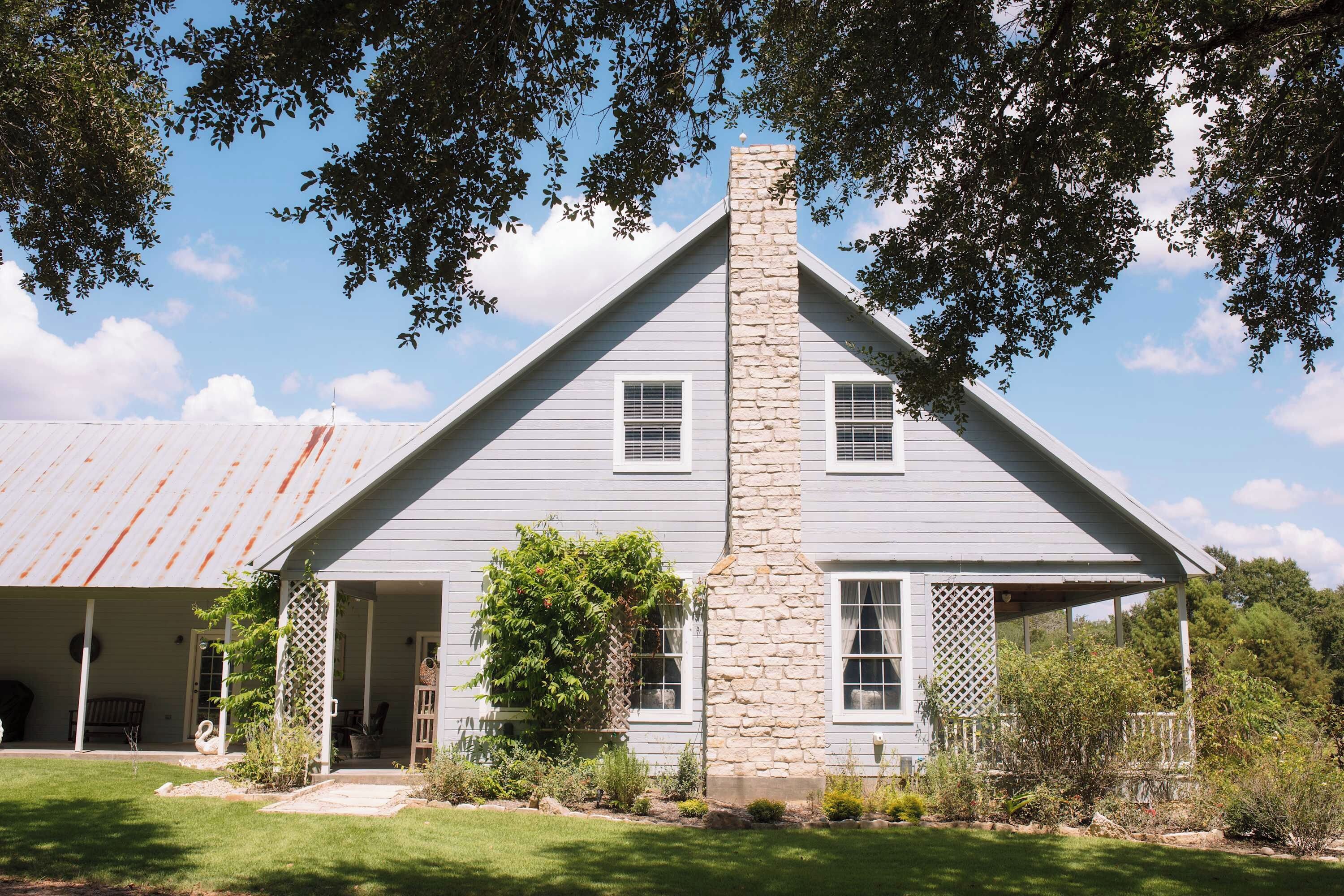 A two-story house with a stone chimney, white siding, and a covered porch.