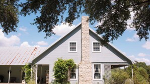 A two-story house with a stone chimney, white siding, and a covered porch. - NEW | Wisteria Ranch | Perfect Round Top Escape (Round Top)